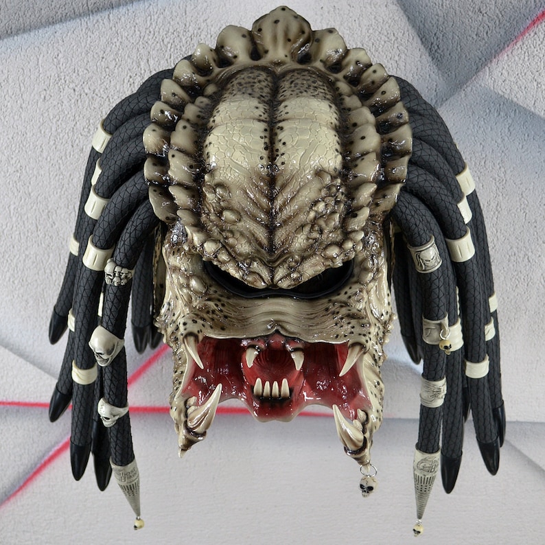 Puede incluir: Un casco de moto de estilo Predator blanco y negro con rastas. El casco tiene una m&aacute;scara facial detallada con dientes afilados y una boca roja.