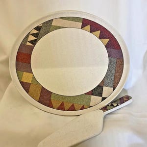 May include: A white ceramic plate and server set. The plate features a geometric border with triangles and rectangles in shades of red, green, yellow, and gray. The server has a matching design on the handle.