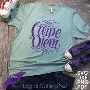 May include: A teal t-shirt with the text "Carpe Diem" in purple script lettering. The shirt is laid out on a wooden surface with a pair of jeans and sneakers.