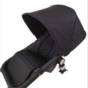 May include: Black stroller seat with a black canopy. The seat has a padded insert and a recline feature. The canopy has a zippered opening for ventilation.