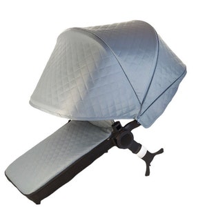 May include: A gray quilted stroller canopy with a black frame and a matching gray footrest. The canopy is fully extended and the footrest is in the down position.