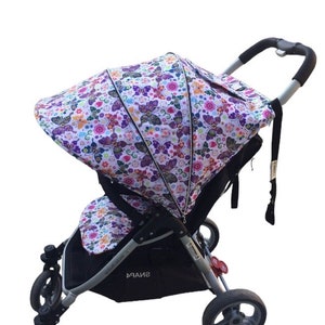 May include: A white stroller with a black frame and purple and pink butterfly patterned canopy. The stroller has a black handle and black wheels. The stroller has the word "SNAP4" printed on the side.