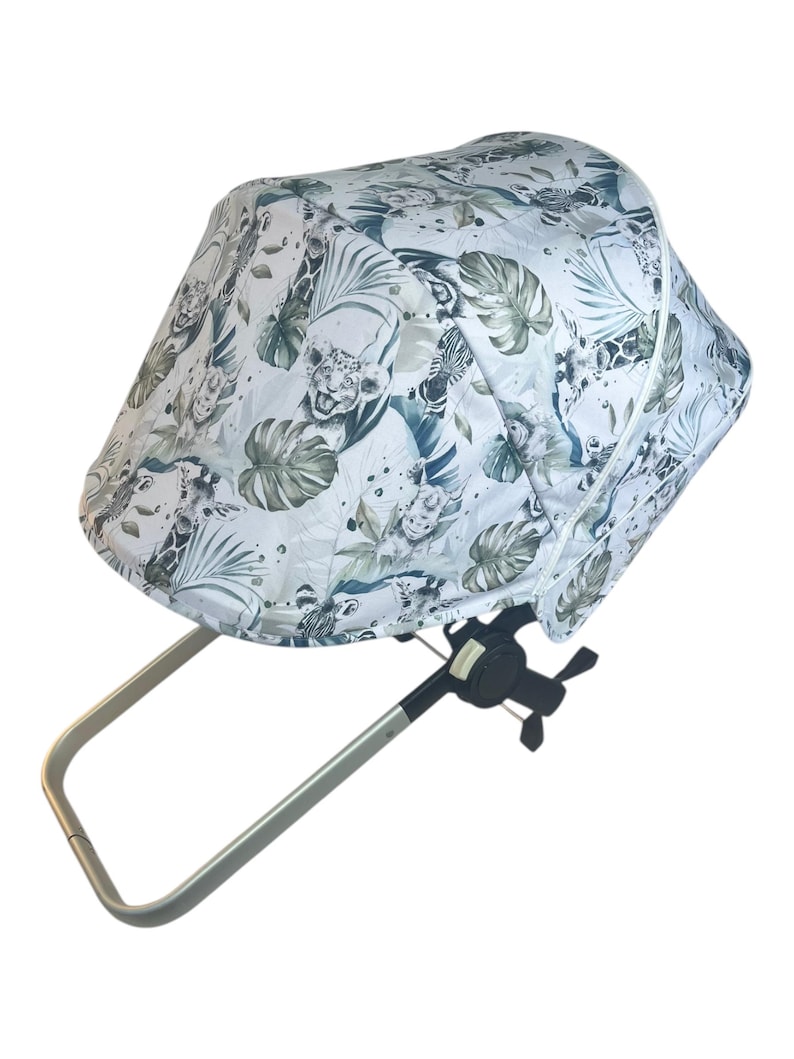 May include: A stroller canopy with a white background and a jungle-themed pattern featuring animals and foliage in shades of green and blue. The canopy is attached to a silver-colored frame.