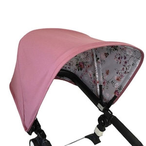 May include: A pink stroller canopy with a floral print lining. The canopy is made of a soft, breathable fabric and provides shade for the baby.