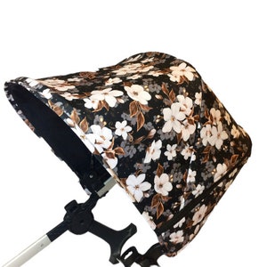 May include: A black stroller canopy with a floral print featuring white flowers and brown leaves on a black background.