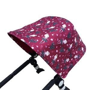 May include: A burgundy stroller canopy with a white and pink floral pattern. The canopy has a white trim and a black frame.