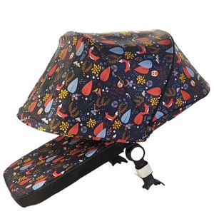 May include: A stroller canopy and bumper bar cover with a dark blue background and a repeating pattern of foxes, leaves, and flowers in red, orange, yellow, and blue. The canopy is angled, and the bumper bar cover is flat.