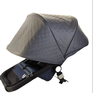 Könnte beinhalten: Ein graues Kinderwagenverdeck mit einem Steppmuster. Das Verdeck ist an einem schwarzen Kinderwagengestell mit Sitz und Griff befestigt. Der Kinderwagen hat einen Sitz aus denimähnlichem Stoff.