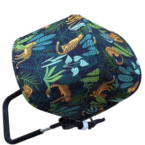 May include: A black stroller canopy with a jungle print featuring green leaves and yellow leopards.