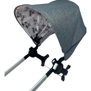 May include: A gray stroller canopy with a white and gray patterned lining. The canopy is attached to a black stroller frame.