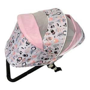 May include: A pink and gray stroller canopy with a feather print design. The canopy has a mesh panel for ventilation.