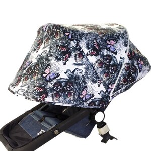 May include: White stroller canopy with a black and white butterfly and floral print. The canopy has a white trim and a white zipper.