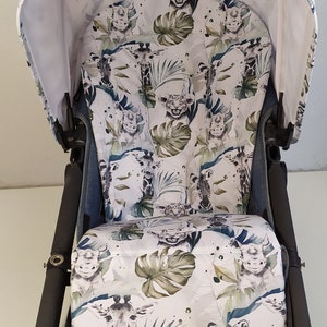May include: A stroller with a white canopy and seat featuring a jungle animal print. The print includes giraffes, zebras, lions, and tropical leaves in shades of green and blue. The stroller frame is black.