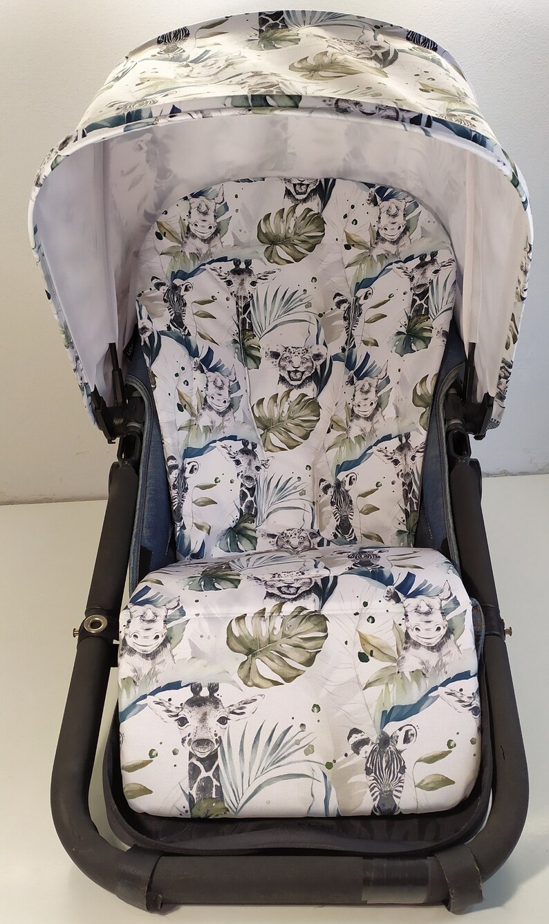 May include: A stroller with a white canopy and seat featuring a jungle animal print. The print includes giraffes, zebras, lions, and tropical leaves in shades of green and blue. The stroller frame is black.