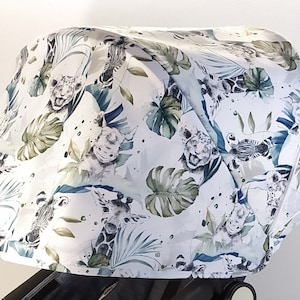 May include: A white stroller canopy featuring a jungle-themed pattern. The design includes illustrations of giraffes, zebras, tigers, and tropical foliage in shades of green and blue. The canopy is attached to a black stroller frame.