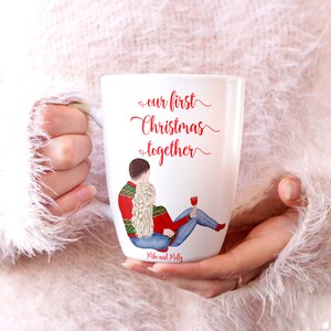 May include: White ceramic mug featuring a red and green illustration of a couple wearing winter sweaters. The text "our first Christmas together" is written in red cursive. The names "Mike and Molly" are written in black at the bottom of the mug.