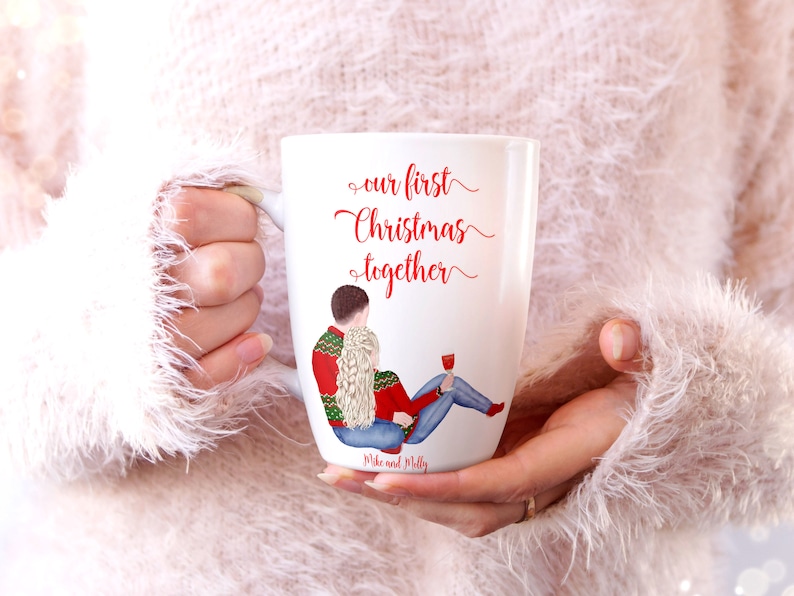 May include: White ceramic mug featuring a red and green illustration of a couple wearing winter sweaters. The text "our first Christmas together" is written in red cursive. The names "Mike and Molly" are written in black at the bottom of the mug.