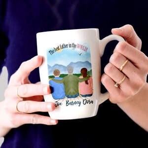 May include: White ceramic mug featuring a colourful illustration of three people standing together with the text "The best father in the world!" and the names "Joe Barney Dora" printed below the illustration.
