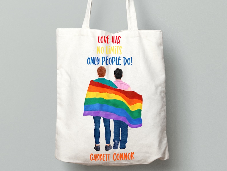 May include: White tote bag with a rainbow flag and two people standing in front of it. The text on the bag reads "Love has no limits only people do!" and "Garrett Connor".