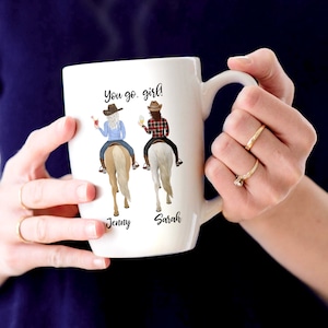 May include: White ceramic mug with a colorful illustration of two women riding horses. The mug has the text "You go girl!" and the names "Jenny" and "Sarah" printed on it.