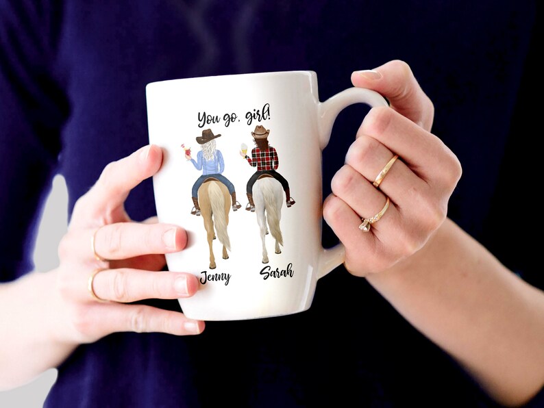 May include: White ceramic mug with a colorful illustration of two women riding horses. The mug has the text "You go girl!" and the names "Jenny" and "Sarah" printed on it.