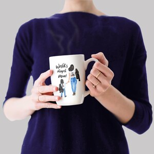 Op de afbeelding: Een witte keramische mok met een zwarte handgreep. De mok heeft een aquarel-illustratie van een moeder en kind die hand in hand lopen. De tekst op de mok is "World's okayest mom!"