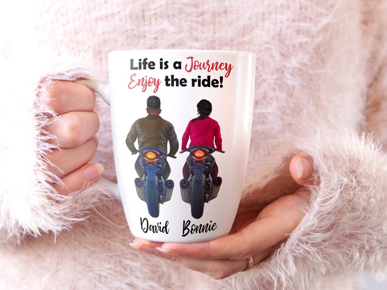 Pu&ograve; includere: Tazza in ceramica bianca con un design nero e rosso. La tazza presenta una coppia in moto con il testo "Life is a Journey Enjoy the ride!" e i nomi "David" e "Bonnie".