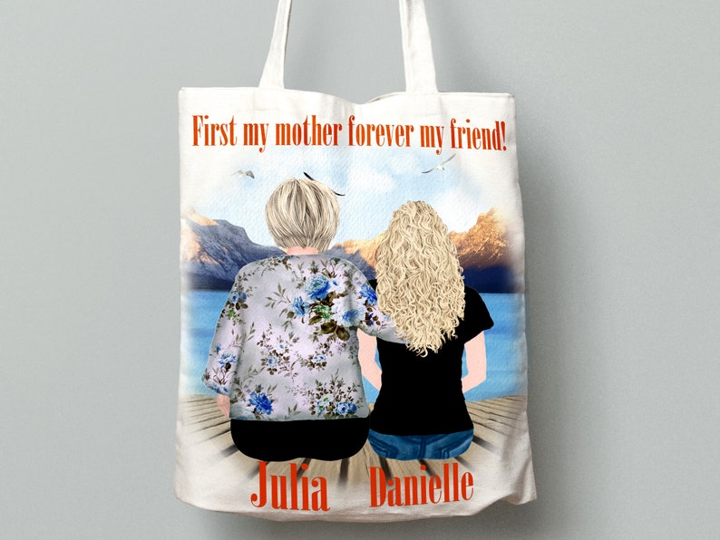 May include: White tote bag with a watercolor illustration of two women sitting on a dock overlooking a lake. The text "First my mother forever my friend!" is printed in orange at the top of the bag. The names "Julia" and "Danielle" are printed at the bottom of the bag.