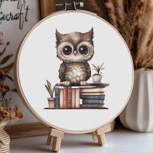 May include: A brown and white owl with large eyes sits on a stack of books. The owl is looking to the right. There is a small potted plant next to the owl.