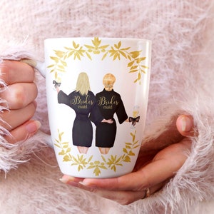 Pode incluir: Caneca de cer&acirc;mica branca com um design floral dourado e duas mulheres em roup&otilde;es pretos com o texto "Brides maid" nas costas de cada roup&atilde;o.
