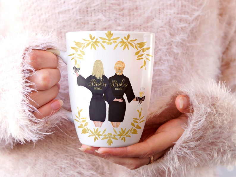 Pode incluir: Caneca de cer&acirc;mica branca com um design floral dourado e duas mulheres em roup&otilde;es pretos com o texto "Brides maid" nas costas de cada roup&atilde;o.