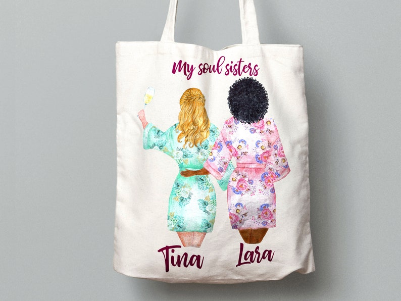 K&ouml;nnte beinhalten: Wei&szlig;e Einkaufstasche mit einer Grafik von zwei Frauen in Roben mit dem Text "my soul sisters" und den Namen "Tina" und "Lara" darunter.