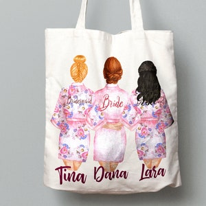 K&ouml;nnte beinhalten: Wei&szlig;e Tragetasche mit drei Frauen in rosa Blumenm&auml;nteln. Die Frauen sind mit "Bride", "Bridesmaid" und "Bridesmaid" beschriftet. Die Namen "Tina", "Dana" und "Lara" sind unten auf der Tasche aufgedruckt.