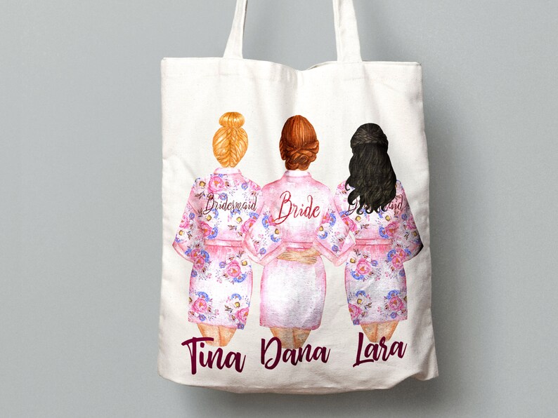 K&ouml;nnte beinhalten: Wei&szlig;e Tragetasche mit drei Frauen in rosa Blumenm&auml;nteln. Die Frauen sind mit "Bride", "Bridesmaid" und "Bridesmaid" beschriftet. Die Namen "Tina", "Dana" und "Lara" sind unten auf der Tasche aufgedruckt.