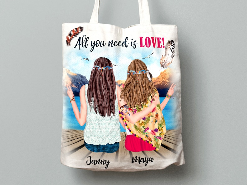 May include: White tote bag with a colorful illustration of two women with long hair and floral headbands sitting on a dock. The text "All you need is LOVE!" is printed in pink and black on the bag. The names "Janny" and "Maya" are printed at the bottom of the bag.