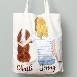May include: A white tote bag with a watercolor illustration of a woman with blonde hair and a brown and white dog. The woman is wearing a blue and white striped shirt and blue jeans. The text "Charli" and "Jenny" is printed on the bag.