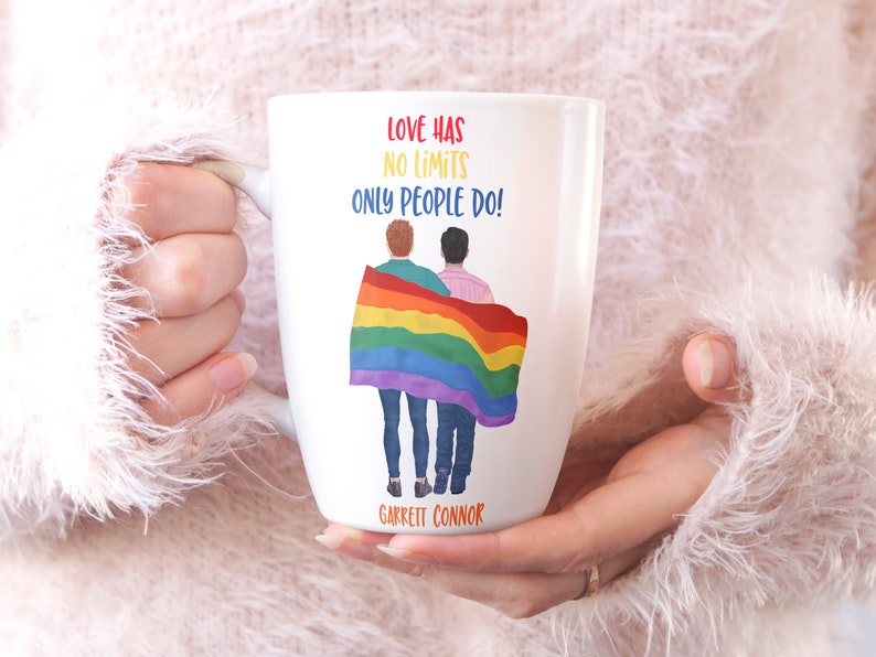 May include: White ceramic mug with a rainbow flag and two people standing in front of it. The text on the mug reads "Love has no limits only people do!" and "Garrett Connor".
