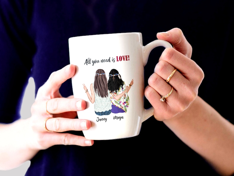 May include: White ceramic mug with a colorful illustration of two women with long hair and floral clothing. The mug has the text "All you need is LOVE!" and the names "Jenny" and "Maya" printed on it.