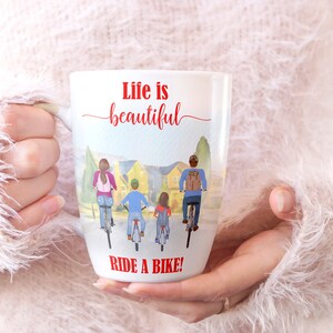 May include: White ceramic mug featuring a watercolor illustration of a family riding bikes. The mug has the text "Life is beautiful" in red script above the illustration and "RIDE A BIKE!" in red block letters below.
