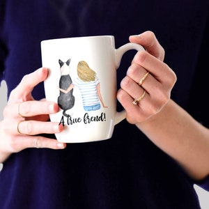May include: White ceramic mug with a watercolor illustration of a woman and a black and white dog sitting back to back. The text "A true friend!" is printed on the mug.