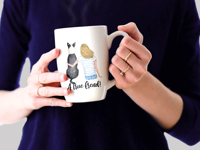 May include: White ceramic mug with a watercolor illustration of a woman and a black and white dog sitting back to back. The text "A true friend!" is printed on the mug.
