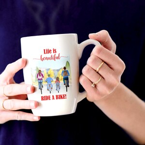 May include: White ceramic mug with a handle, featuring the text "Life is beautiful" in red script above a watercolor illustration of a family riding bikes. The phrase "RIDE A BIKE!" is printed in red below the illustration.