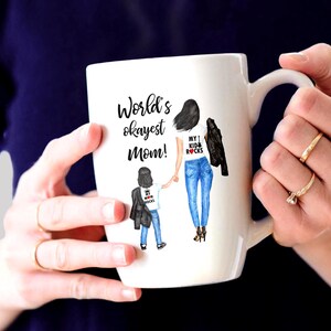 Op de afbeelding: Een witte keramische mok met een zwart-witte illustratie van een moeder en kind. De tekst op de mok luidt "World's okayest Mom!" en "My 1 Kid Rocks".