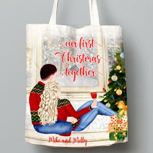May include: A white tote bag with a Christmas-themed design. The design features a couple sitting by a window with a Christmas tree in the background. The text on the bag reads "our first Christmas together" and "Mike and Molly".