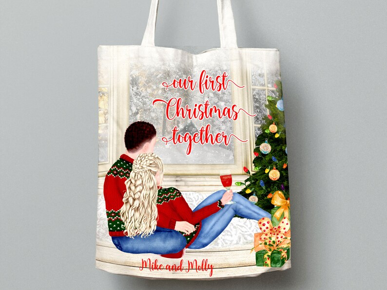 May include: A white tote bag with a Christmas-themed design. The design features a couple sitting by a window with a Christmas tree in the background. The text on the bag reads "our first Christmas together" and "Mike and Molly".