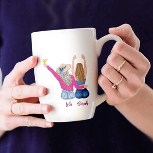 May include: White ceramic mug with a colorful illustration of two women with the names "Lola" and "Sarah" written below.