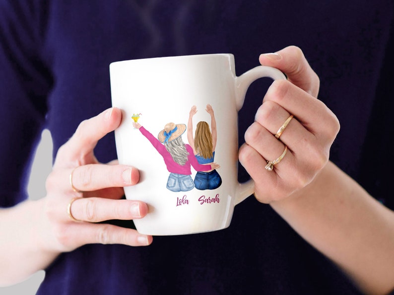 May include: White ceramic mug with a colorful illustration of two women with the names "Lola" and "Sarah" written below.