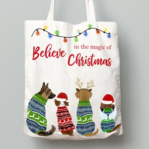 May include: White canvas tote bag with the text "Believe in the magic of Christmas" and a string of Christmas lights. Four dogs wearing Christmas sweaters are sitting in a row at the bottom of the bag.