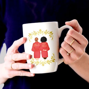 Pode incluir: Caneca de cer&acirc;mica branca com um design floral dourado. Duas mulheres em roup&otilde;es vermelhos s&atilde;o retratadas na caneca, uma com a etiqueta "Bride" e a outra com "Maid of Honor".