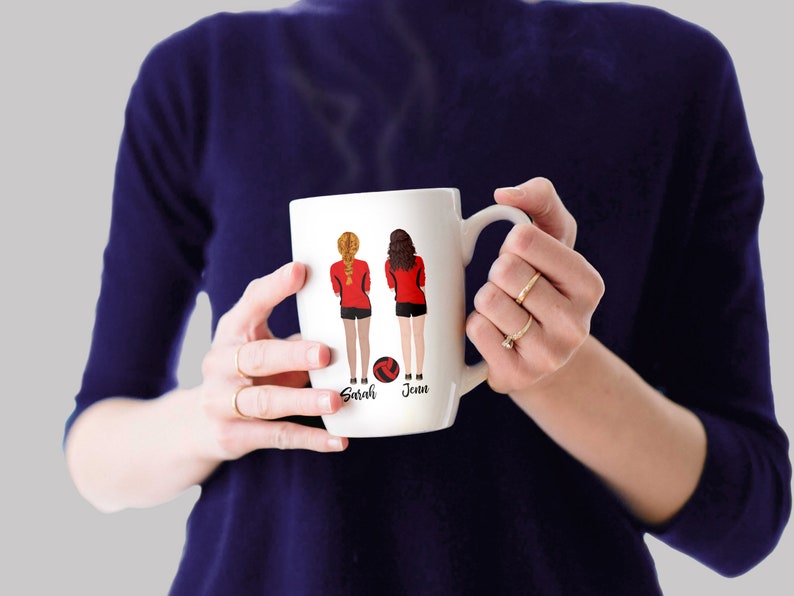 May include: White ceramic mug with a design of two women in red and black volleyball uniforms holding a volleyball. The names "Sarah" and "Jenn" are printed below the women.